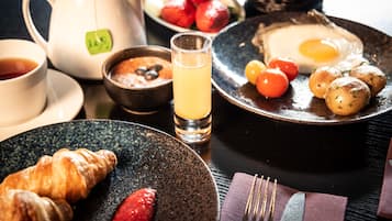 Una mesa para el desayuno con tetera, tazas, un vaso de jugo, croissants, fresas y un plato con huevos y tomates.