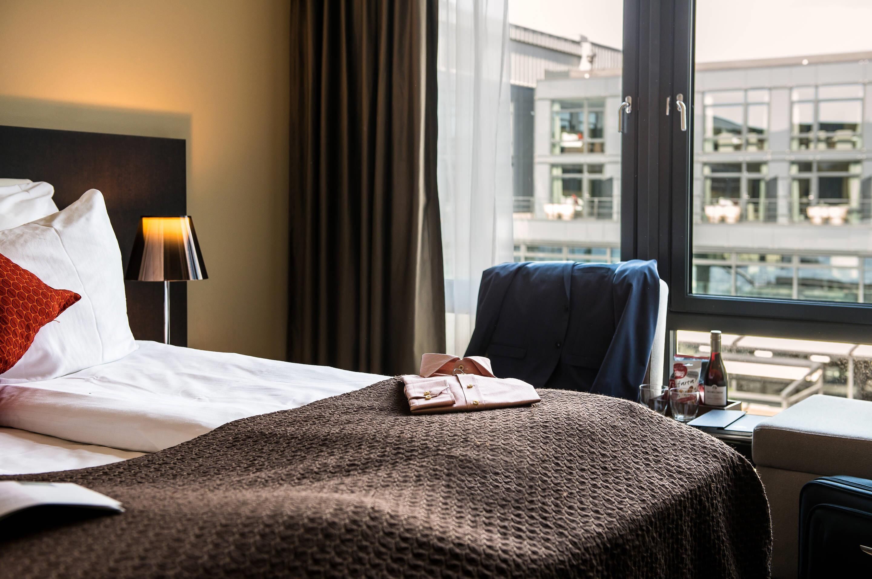 A hotel room with a bed, a desk, and a window with a view of a building.
