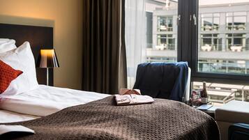 A hotel room with a bed, a desk, and a window with a view of a building.