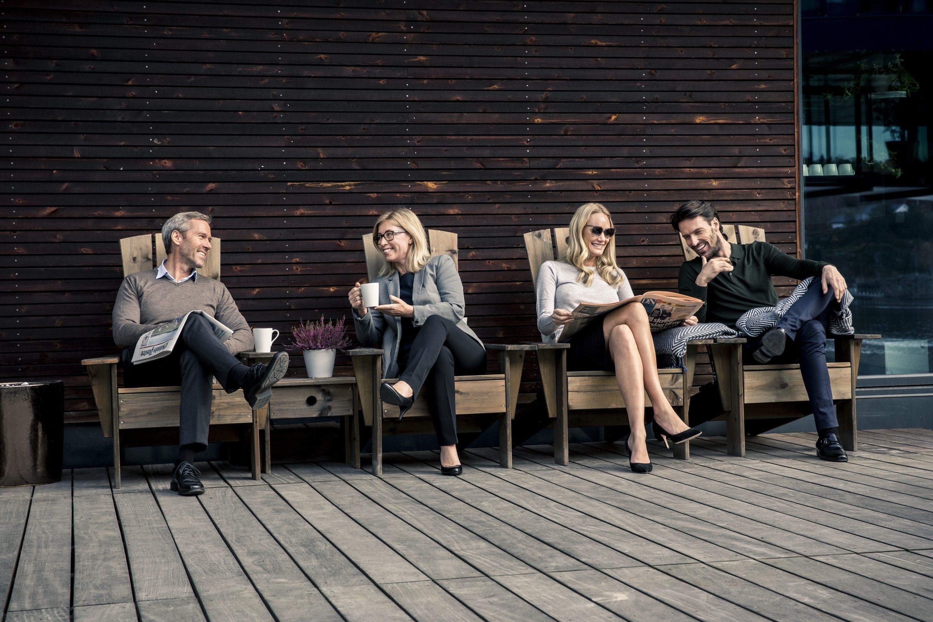 Four people seated on wooden benches against a dark wooden wall, with a wooden deck in the foreground.