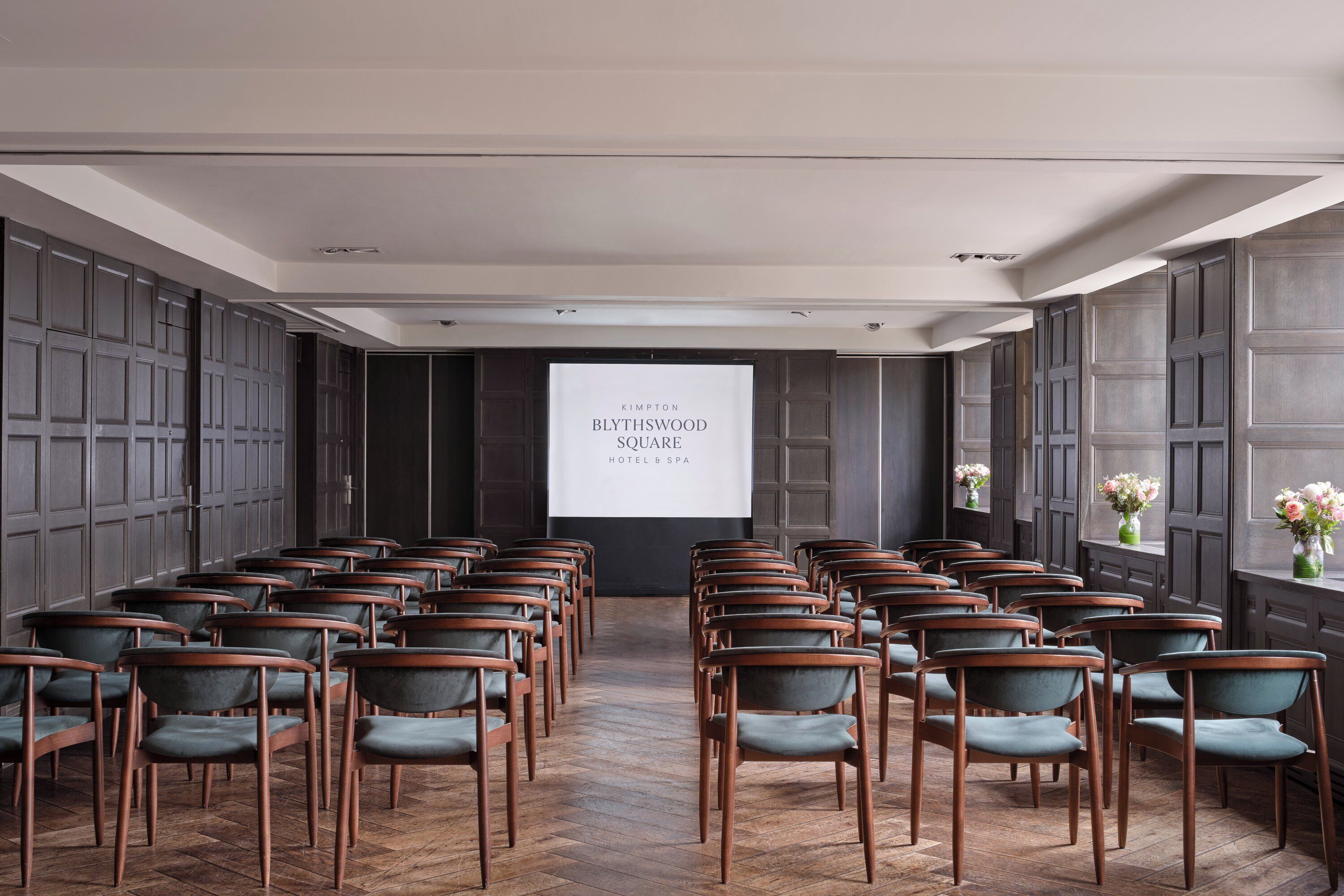A conference room with rows of chairs, a projection screen, and dark wood paneling.