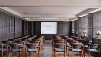 A conference room with rows of chairs, a projection screen, and dark wood paneling.