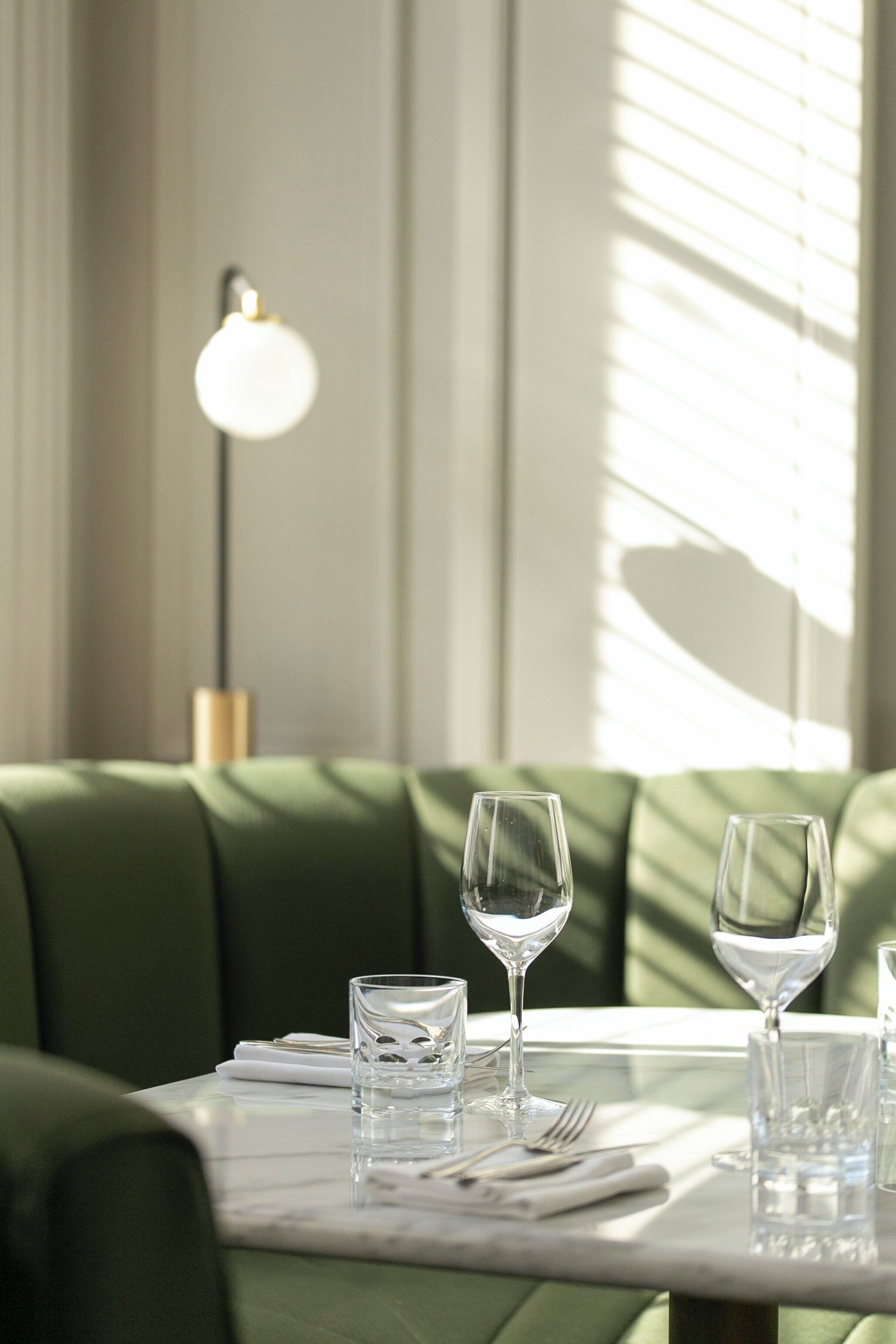 A dining table with a green upholstered bench, two wine glasses, and a lamp in the background.