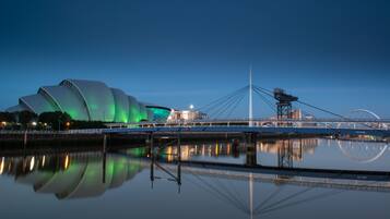 A modern bridge with a unique cable design, a large green-lit building, and a calm water body reflecting the structures.