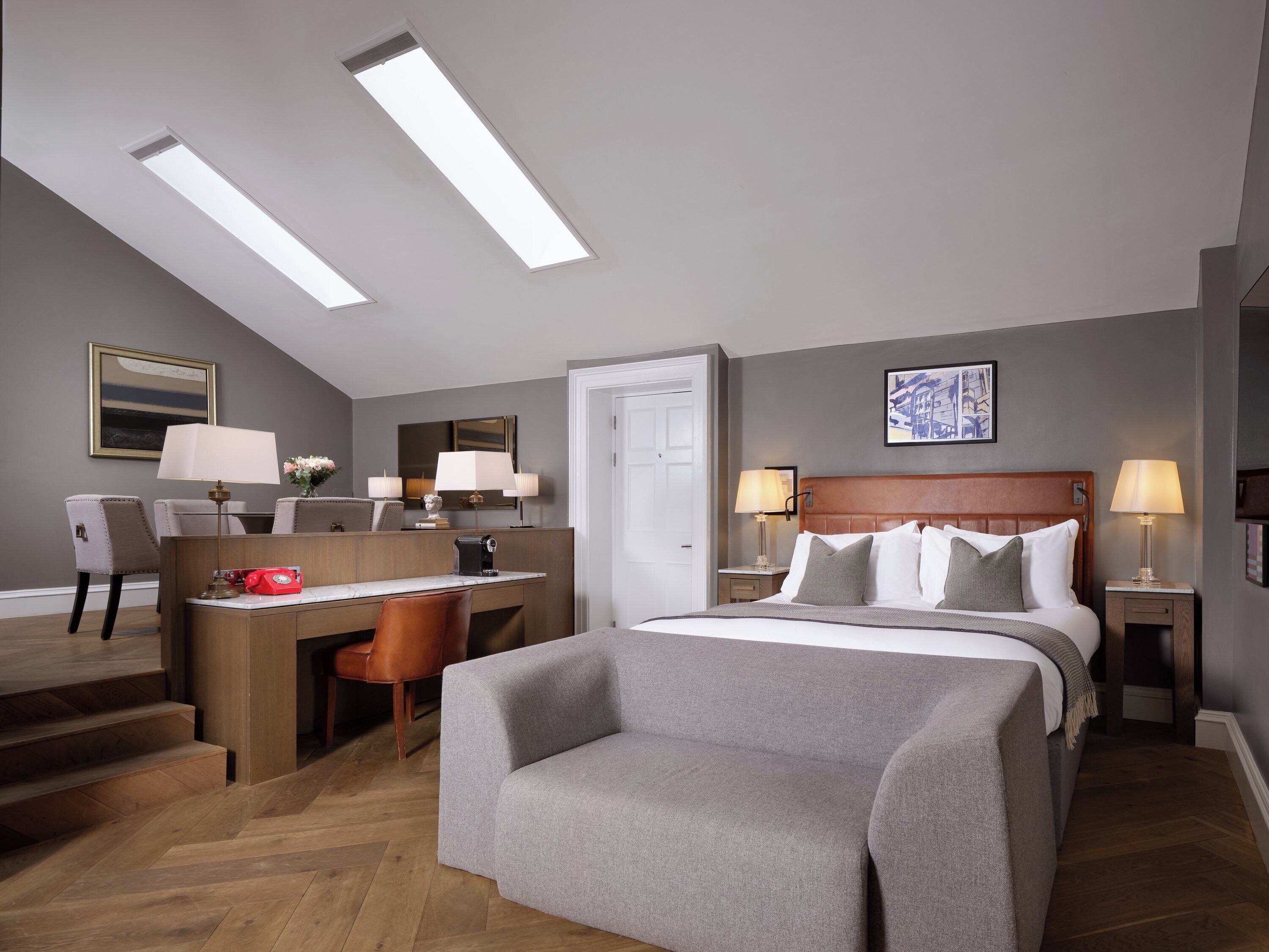 A hotel room with a bed, desk, chair, and a view of the sky through skylights.