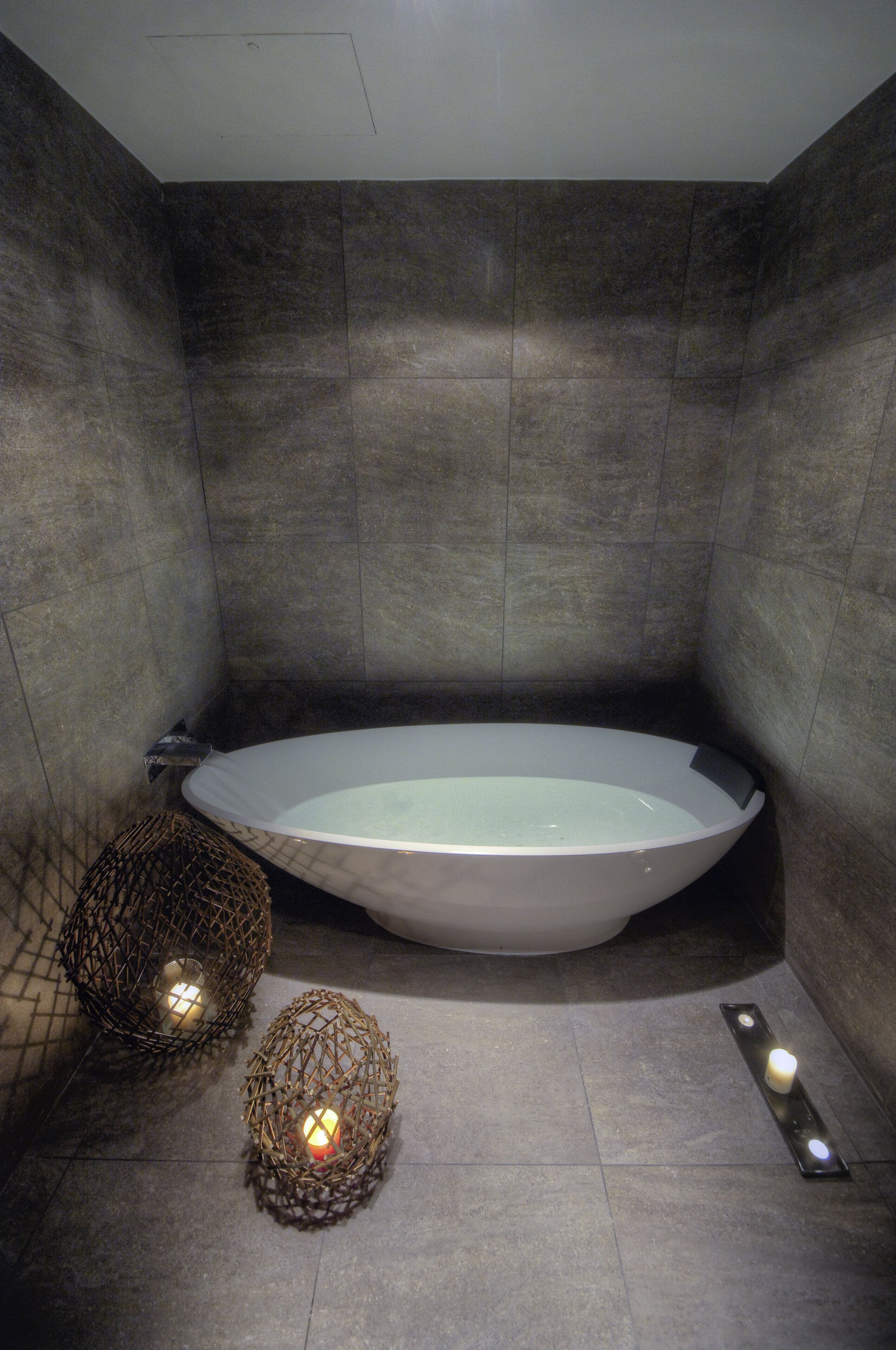 A modern bathroom with a freestanding bathtub, two decorative candle holders, and a wall-mounted light fixture.