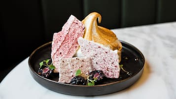 A dessert plate with a meringue, a pink cake, and blackberries on a dark plate.