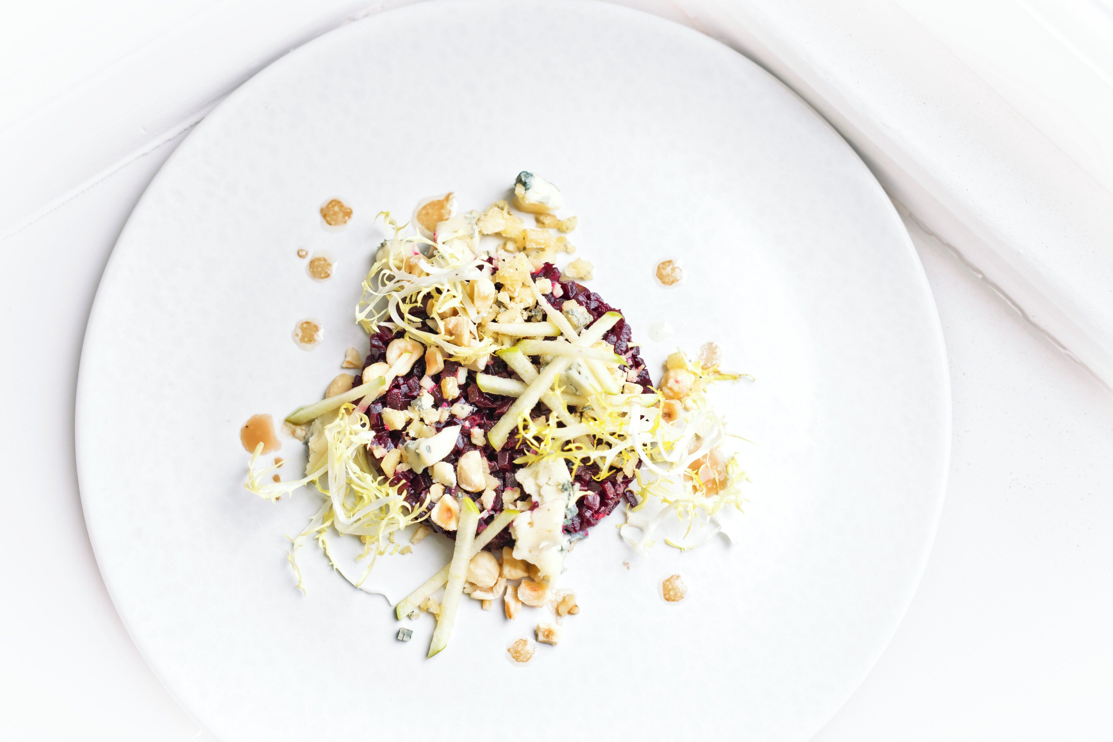 A white plate with a salad consisting of shredded vegetables and nuts.
