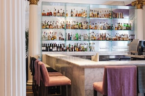 A bar area with multiple shelves of liquor bottles, bar stools, and a marble countertop.