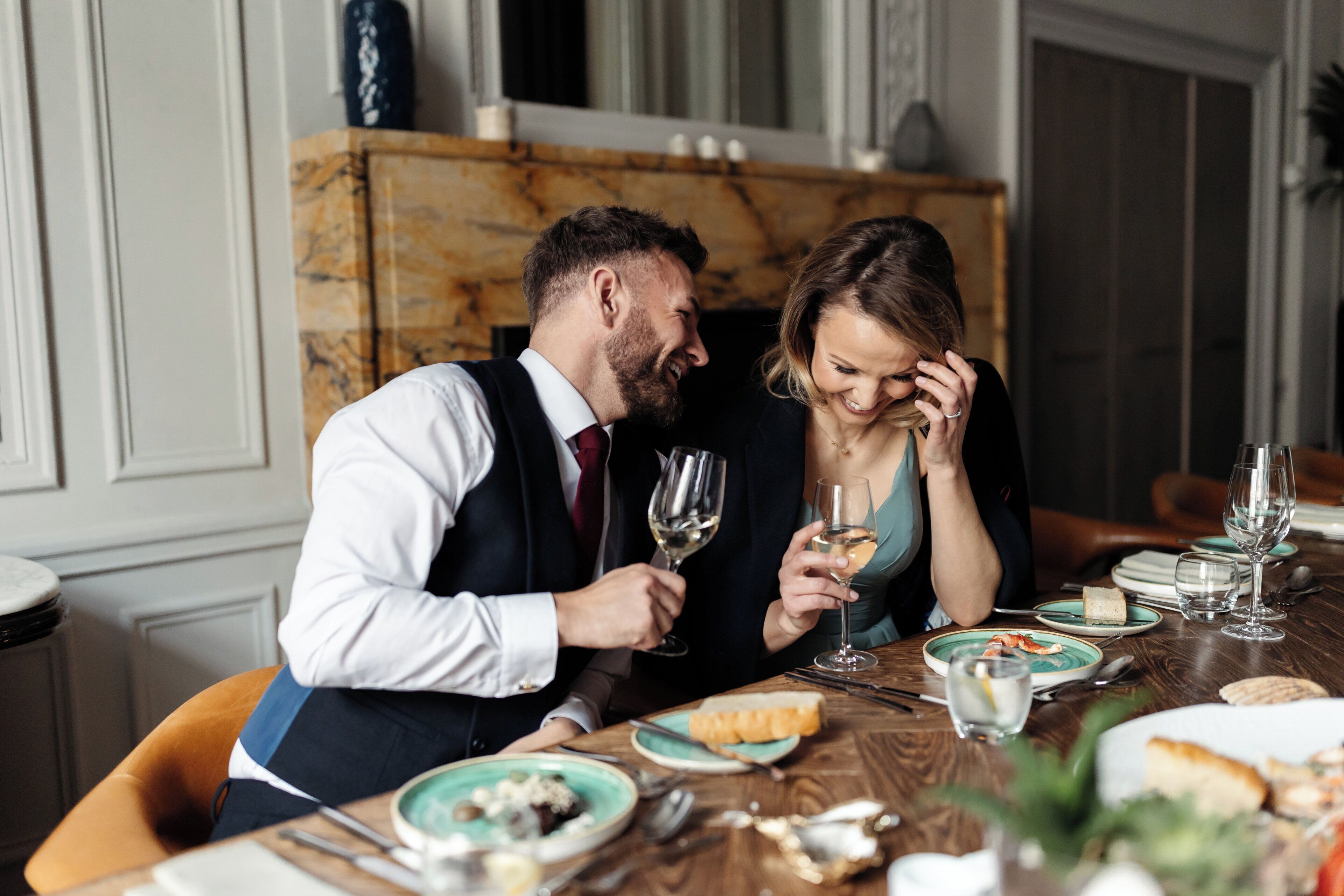 Una pareja cenando en una mesa con platos de comida y copas de vino, con una chimenea de mármol al fondo.