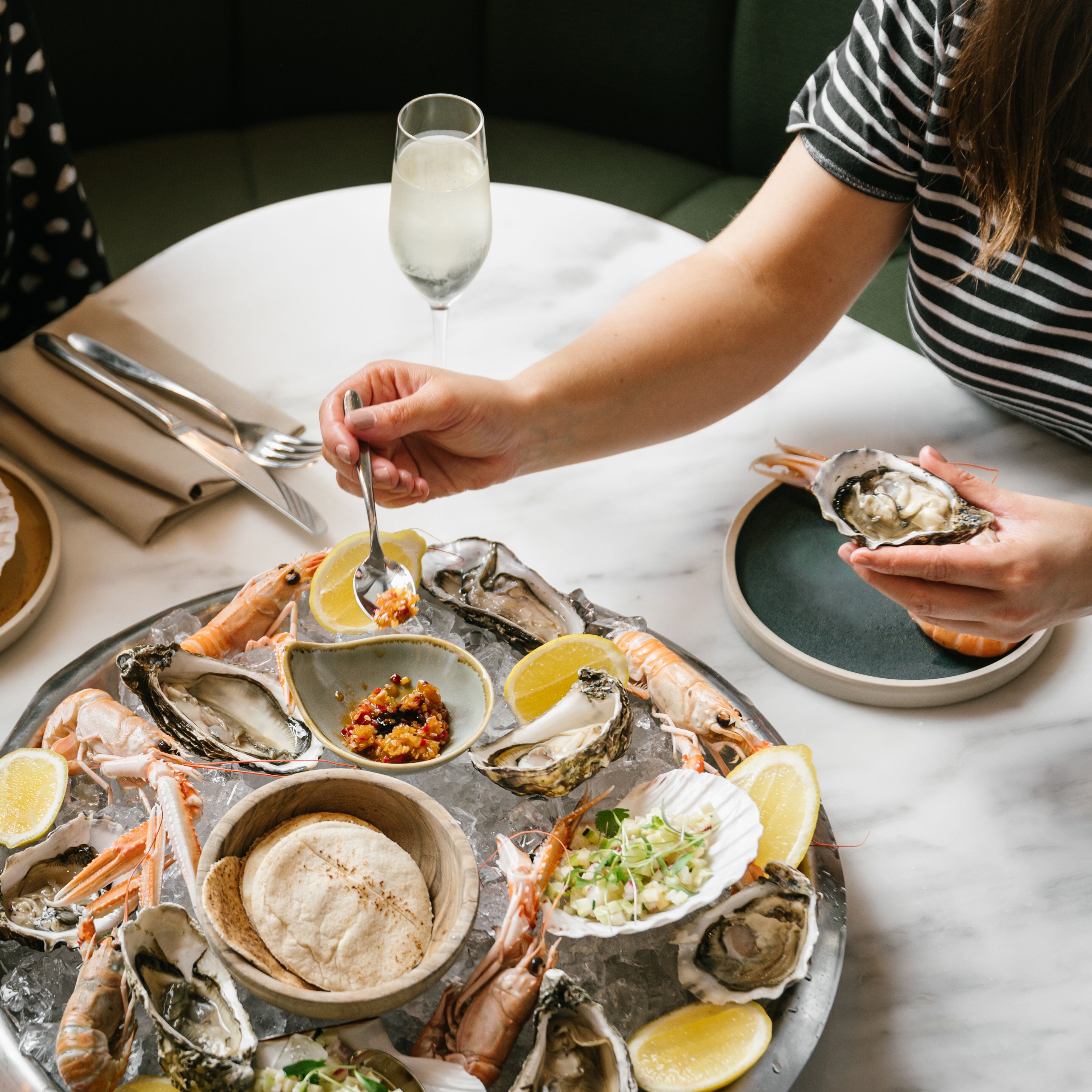 Een plateau vol zeevruchten met diverse schelpdieren en een glas witte drank op een marmeren tafel.