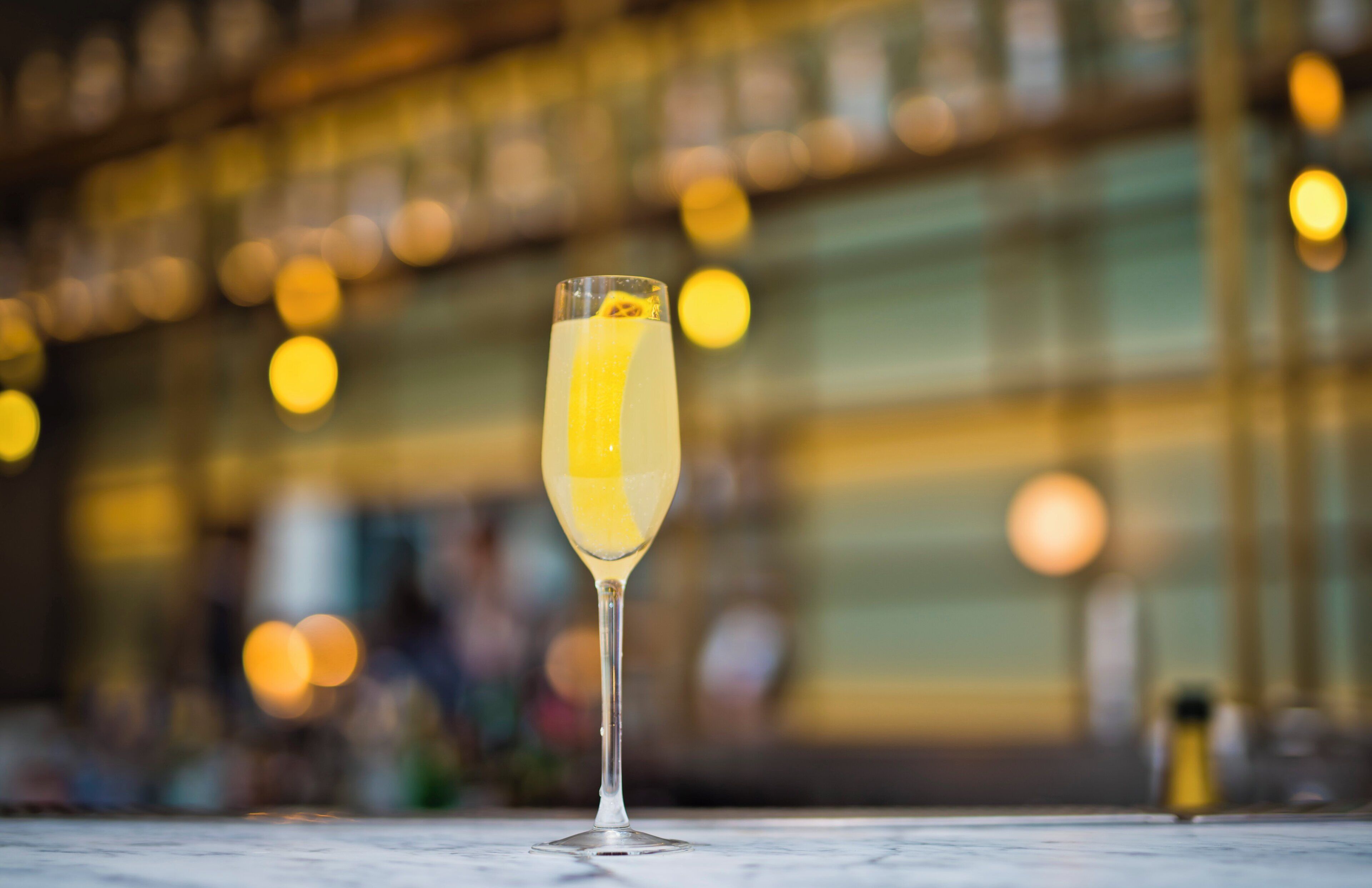 A clear glass of a yellow beverage on a marble surface with a blurred background of lights.