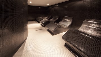 Relax in a serene spa room with reclining chairs, footrests, and headrests, set against a patterned tile floor and mosaic walls.