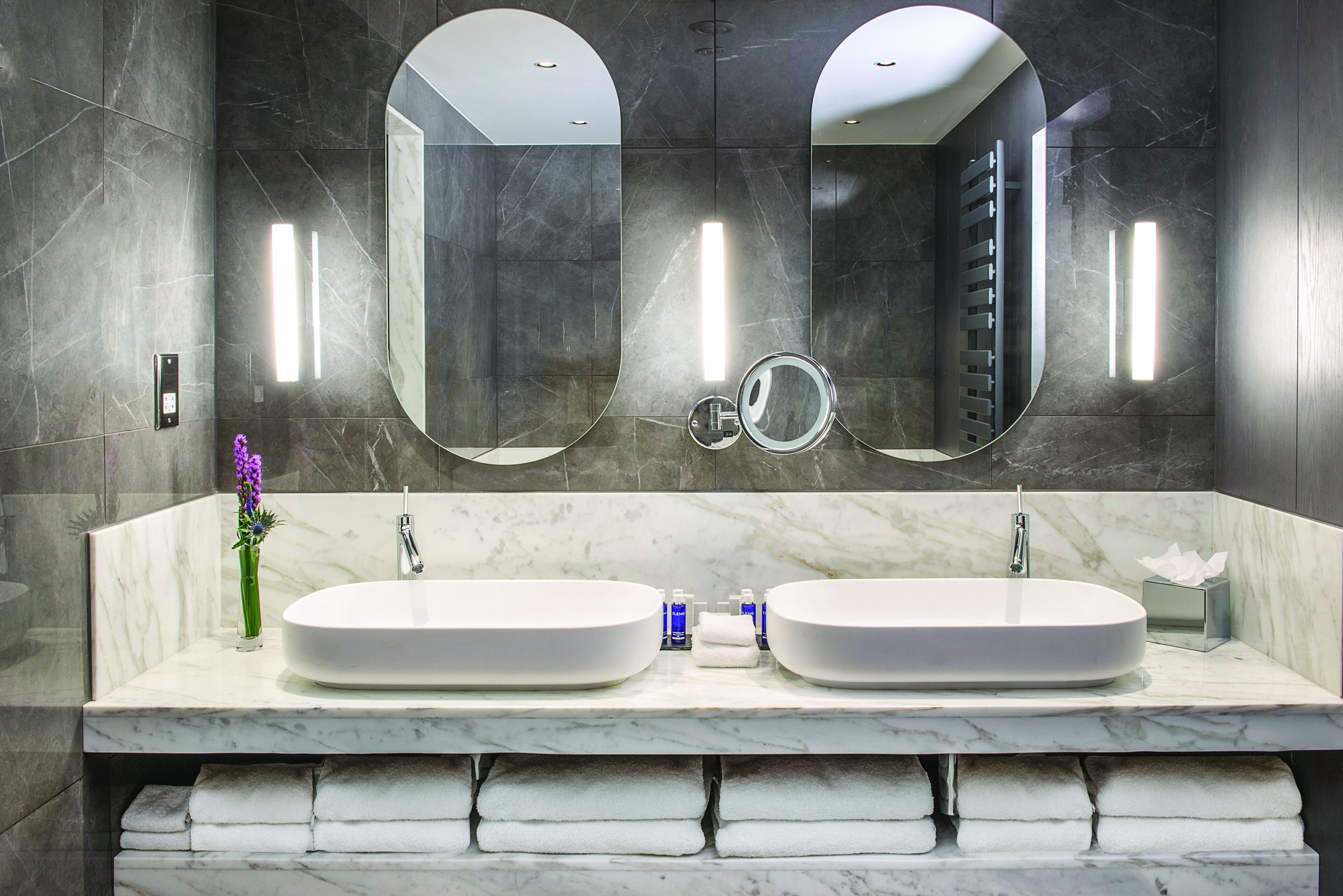 A modern bathroom with two sinks, a large mirror, and a towel rack.