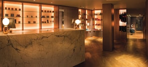 A hotel lobby with a marble reception desk, shelves with toiletries, and a clothing rack.