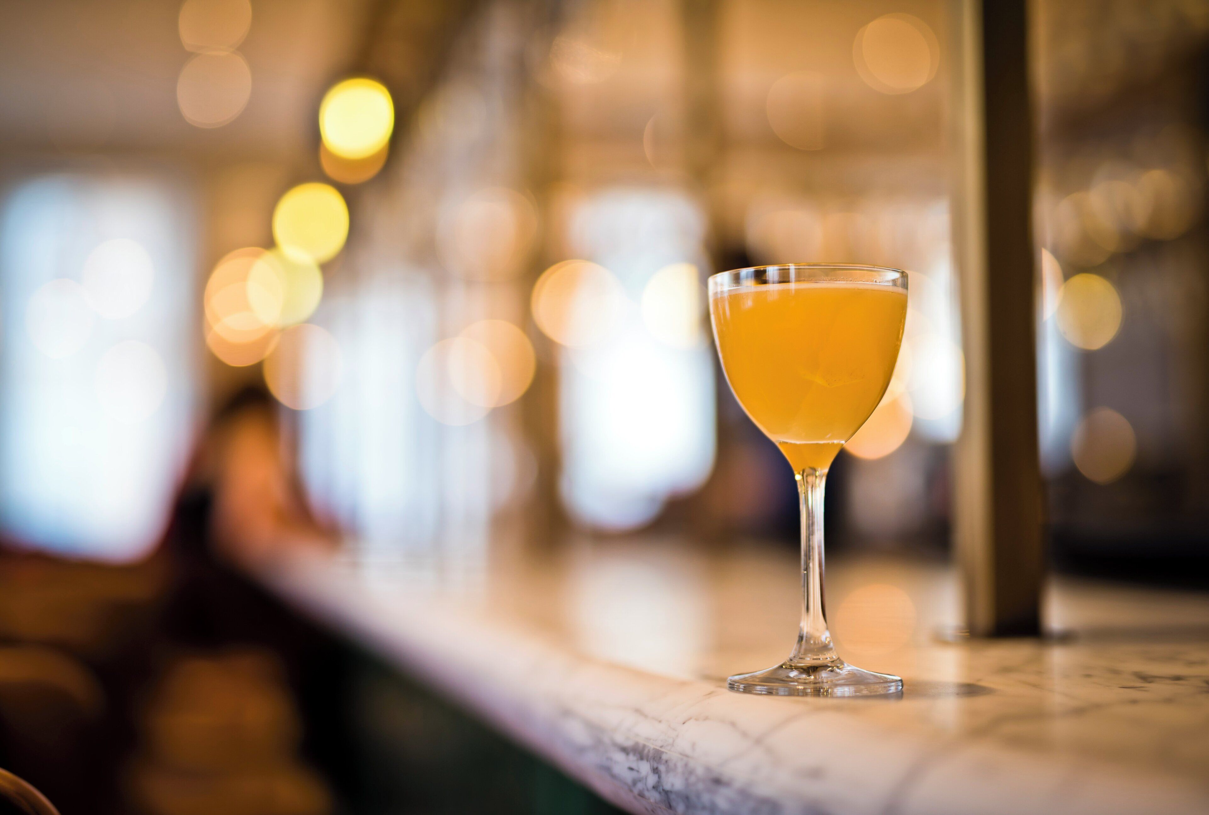 A cocktail glass on a bar counter with blurred lights in the background.