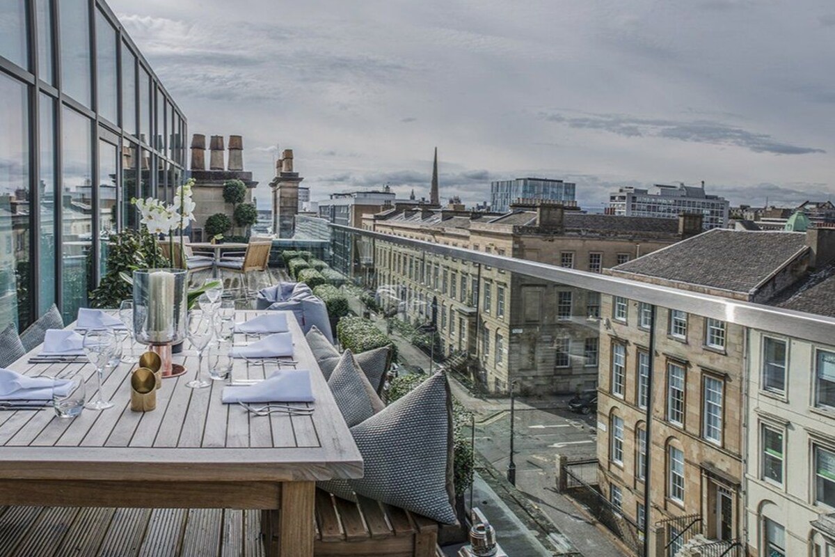 A dining area with a table set for two, overlooking a cityscape with historic buildings and a modern skyscraper.