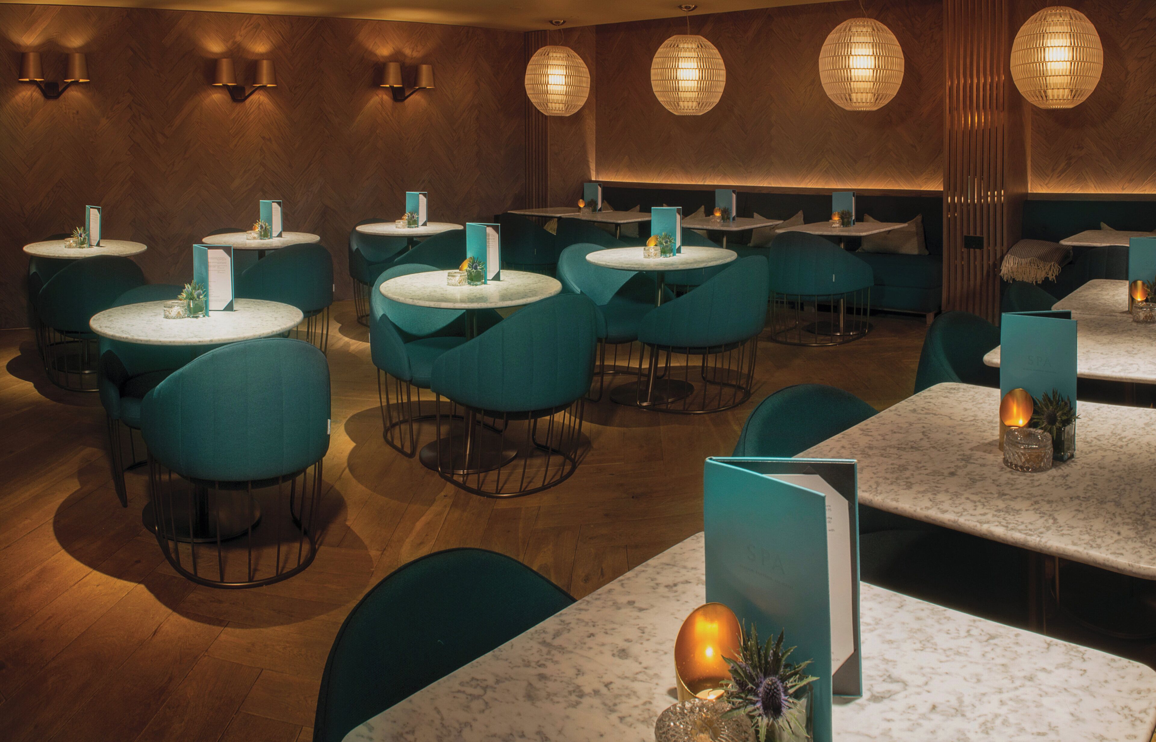 Un interior de restaurante con mesas redondas, sillas color turquesa e iluminación colgante.