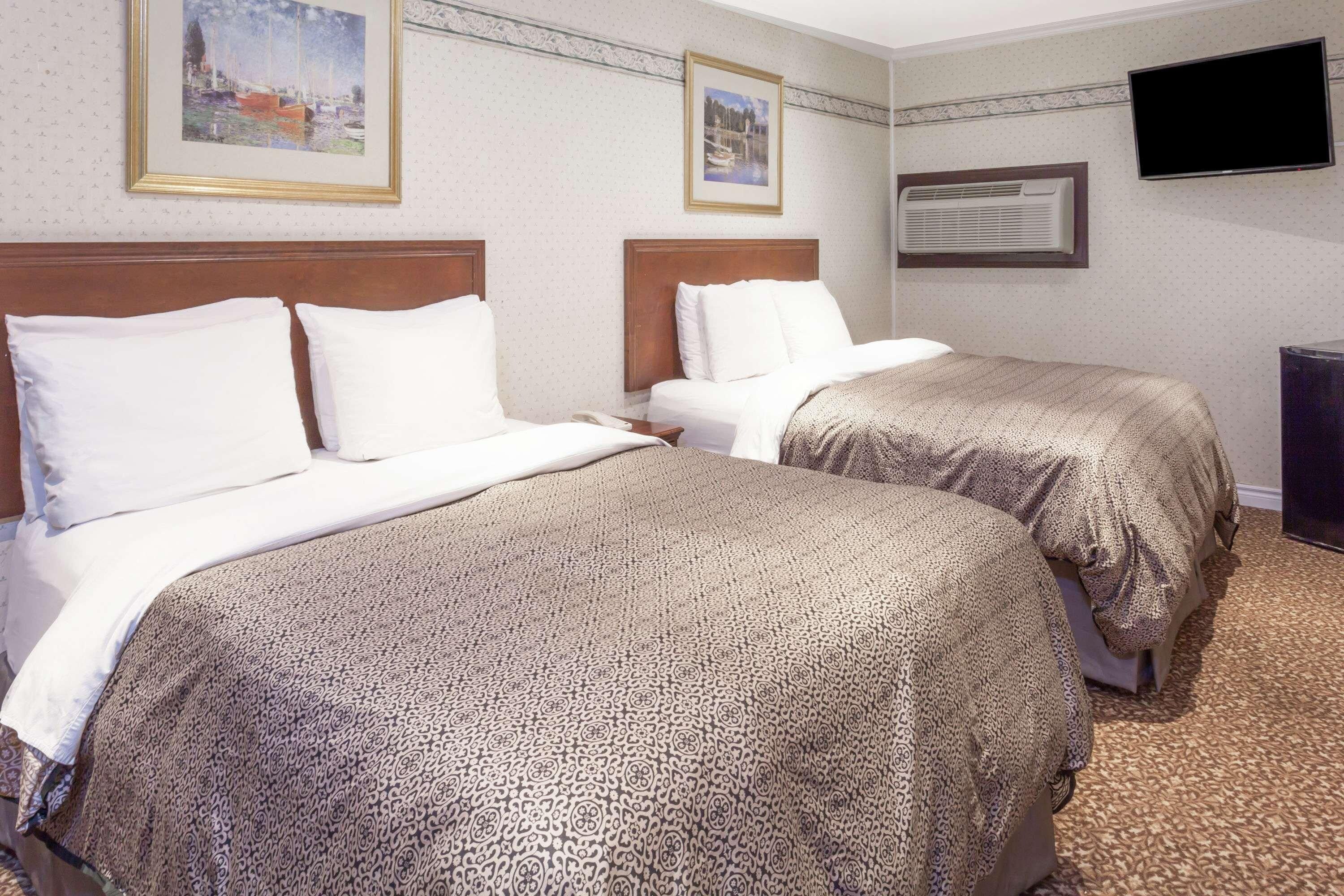 A hotel room with two beds, a television, and artwork on the walls.