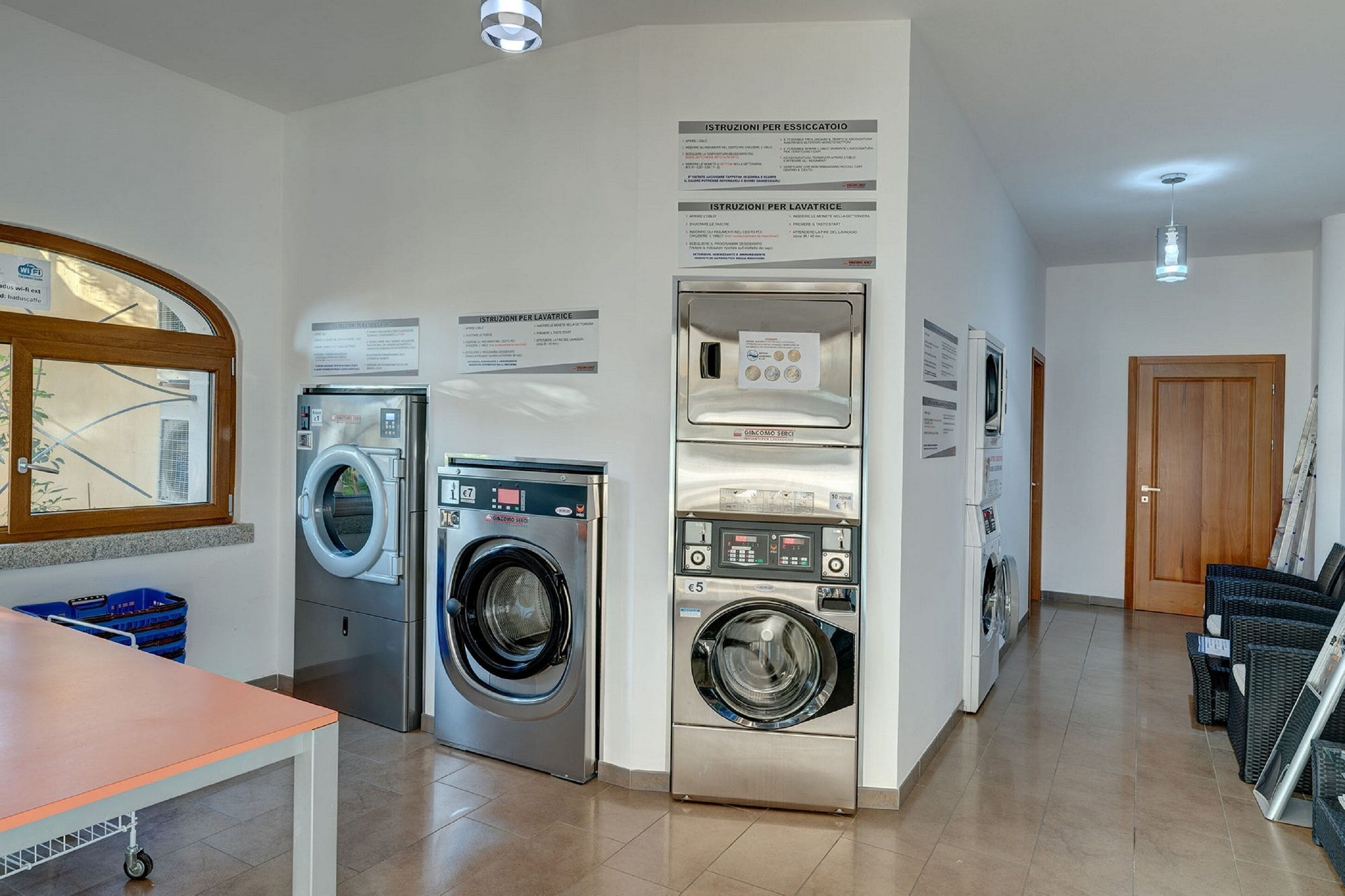 A laundry facility with multiple washing machines and dryers, instructional signs, and a wooden door.