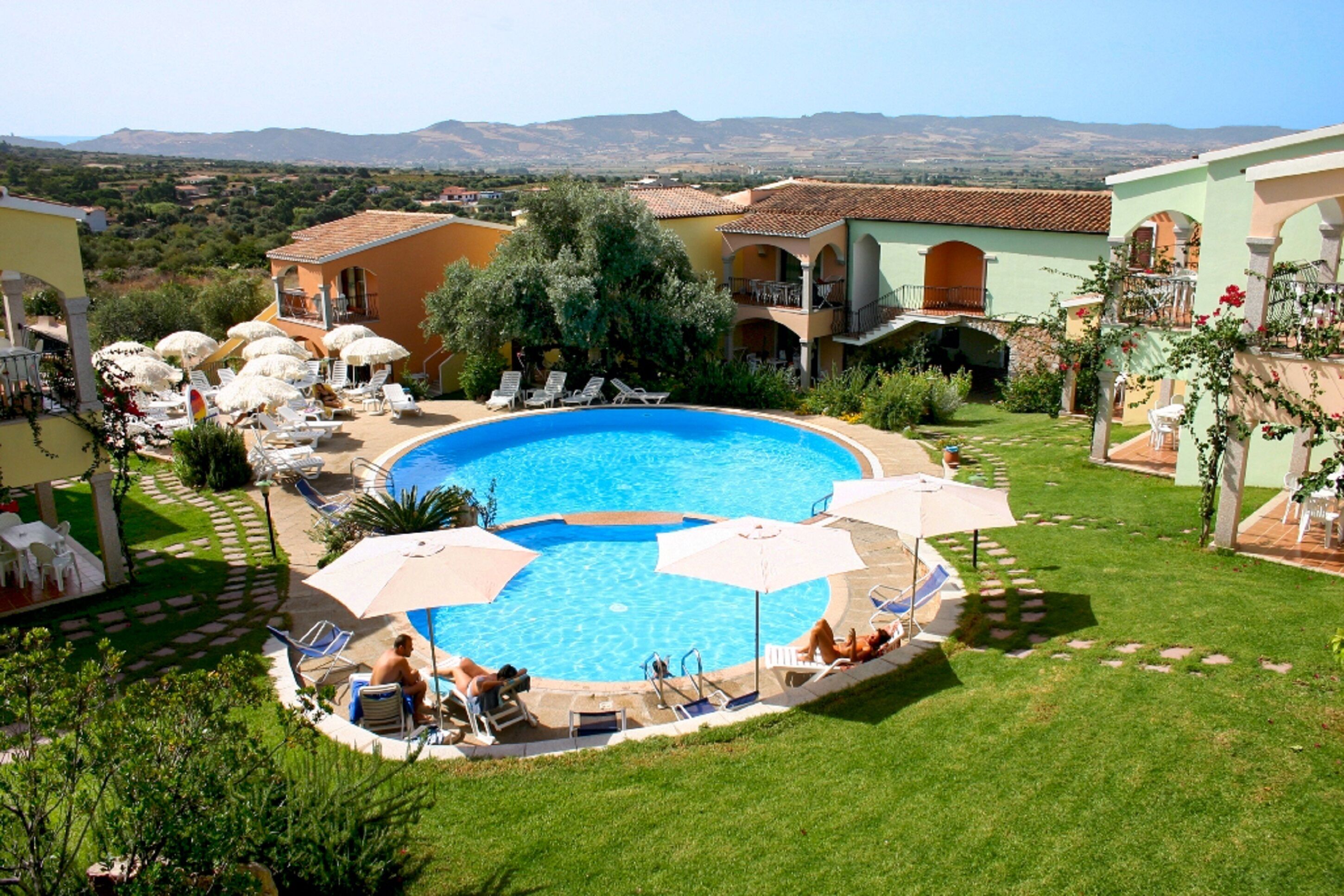 A pool area with lounge chairs and umbrellas, surrounded by buildings with Mediterranean architecture.