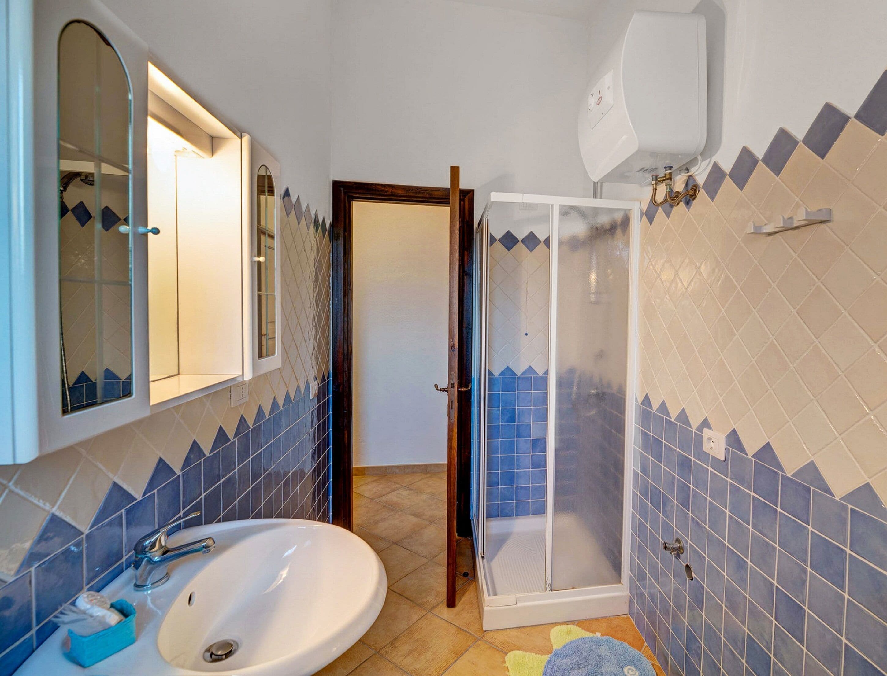 A bathroom with a sink, mirror, shower, and tiled walls.
