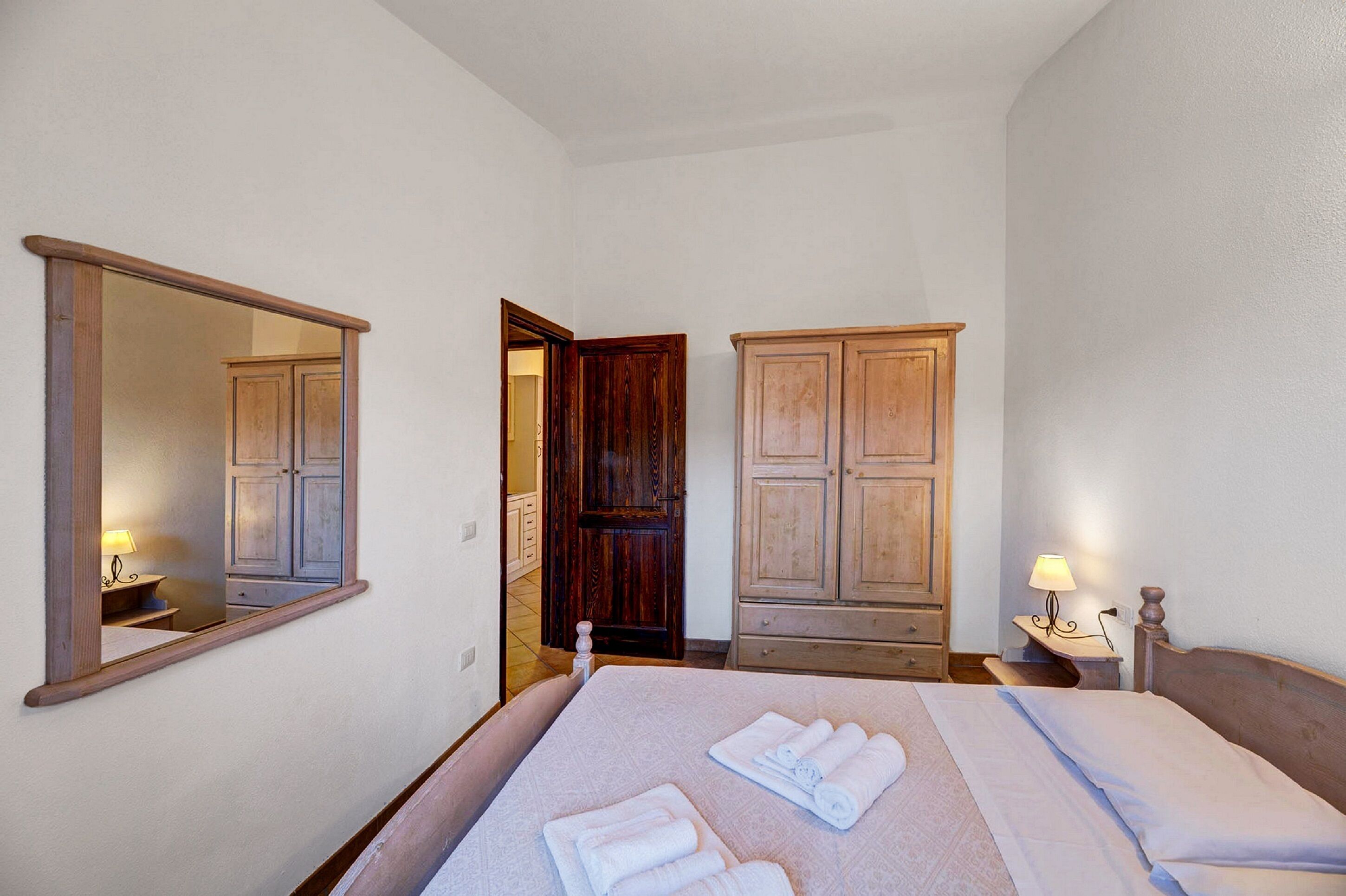 Una habitación de hotel con una cama, un espejo, un armario y una mesita de noche con lámpara.