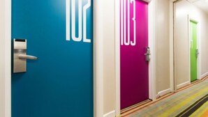 Un couloir d’hôtel avec les portes numérotées 102 et 103, une moquette rayée aux couleurs vives et une poignée de porte moderne.