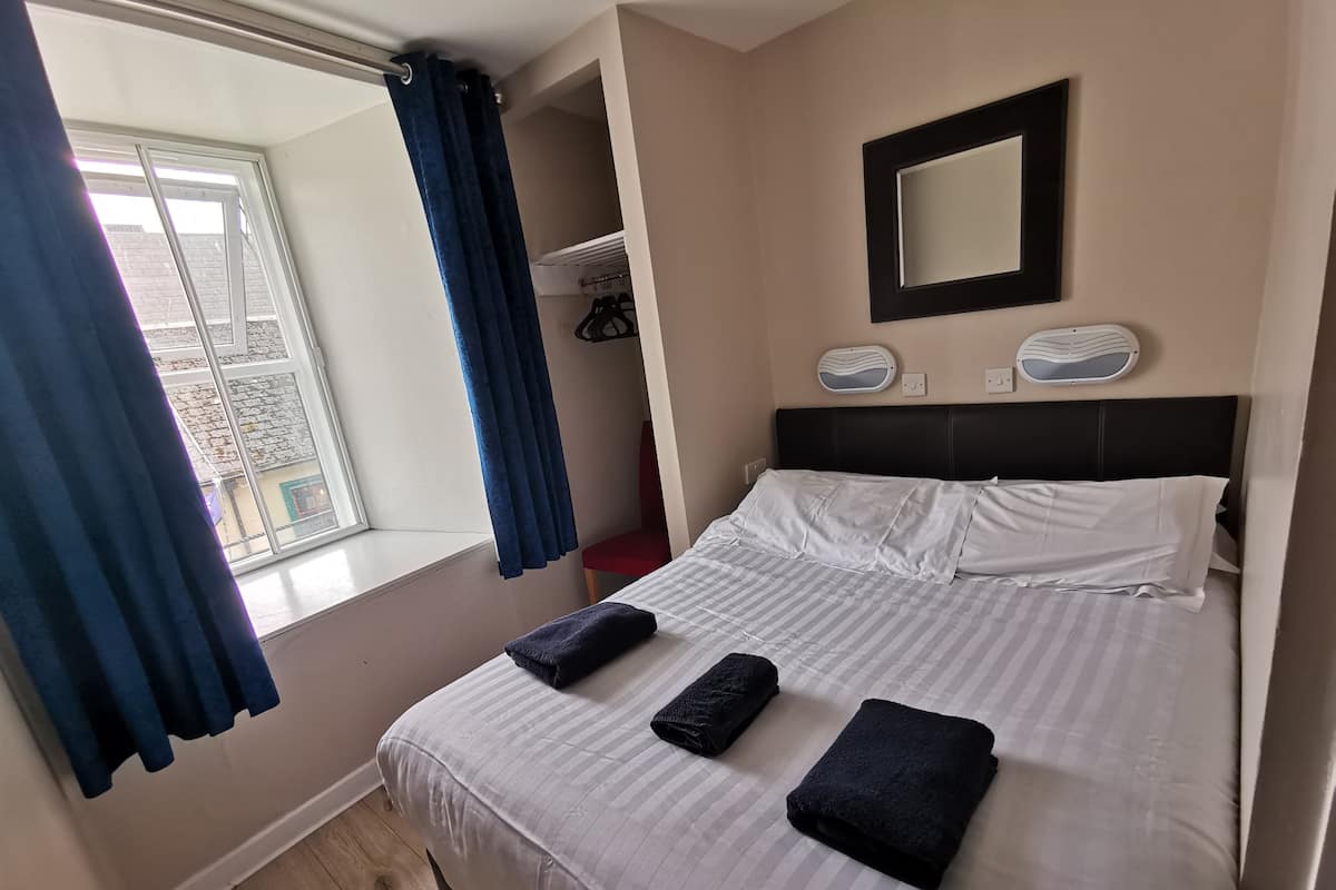 Ein Hotelzimmer mit Bett, einem Vorhangfenster, einem Kopfteil, einem Spiegel und einem Wandventilator.
