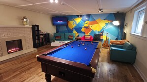 Une table de billard dans une pièce dotée d’une cheminée, d’une fresque représentant une carte du monde et d’un téléviseur diffusant du contenu de « Netflix ».