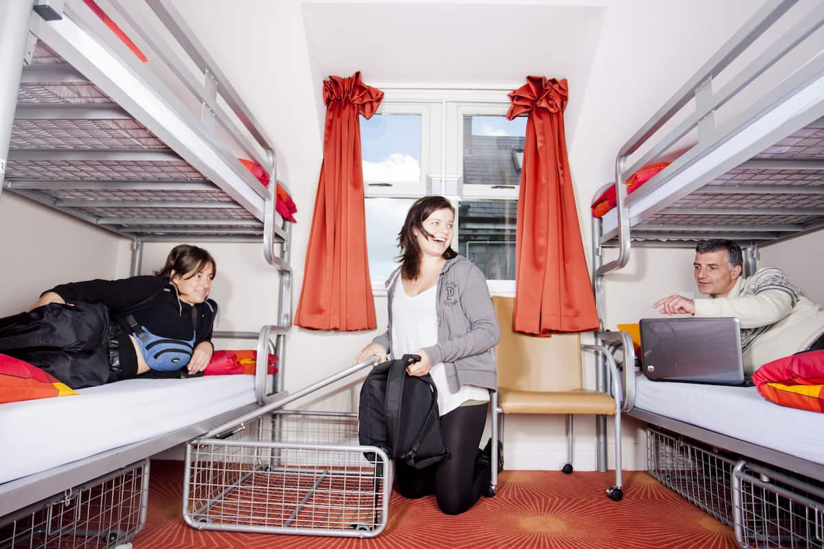 Ein Schlafsaalzimmer mit Etagenbetten, einem Fenster mit Vorhängen und einem Laptop auf einem Bett.
