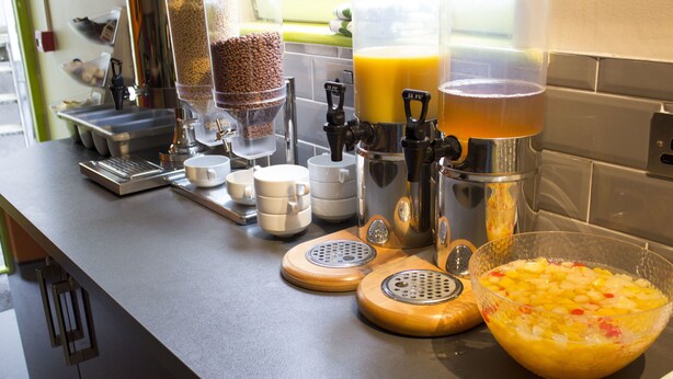 Un plan de travail de cuisine avec des machines à café, un moulin à café, un panier de fruits et un distributeur de café.