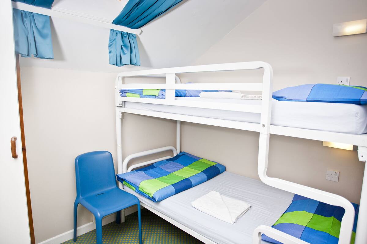 Ein Stockbett mit blauem Stuhl, einer weißen Tür und einem Lichtschalter an der Wand.