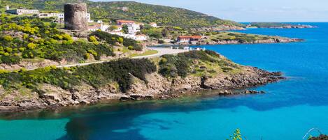 A coastal town with a prominent tower, houses, and a clear blue sea.