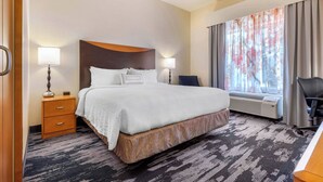 Quarto de hotel com uma cama grande, duas mesas de cabeceira com abajures, uma escrivaninha e uma janela com cortinas.