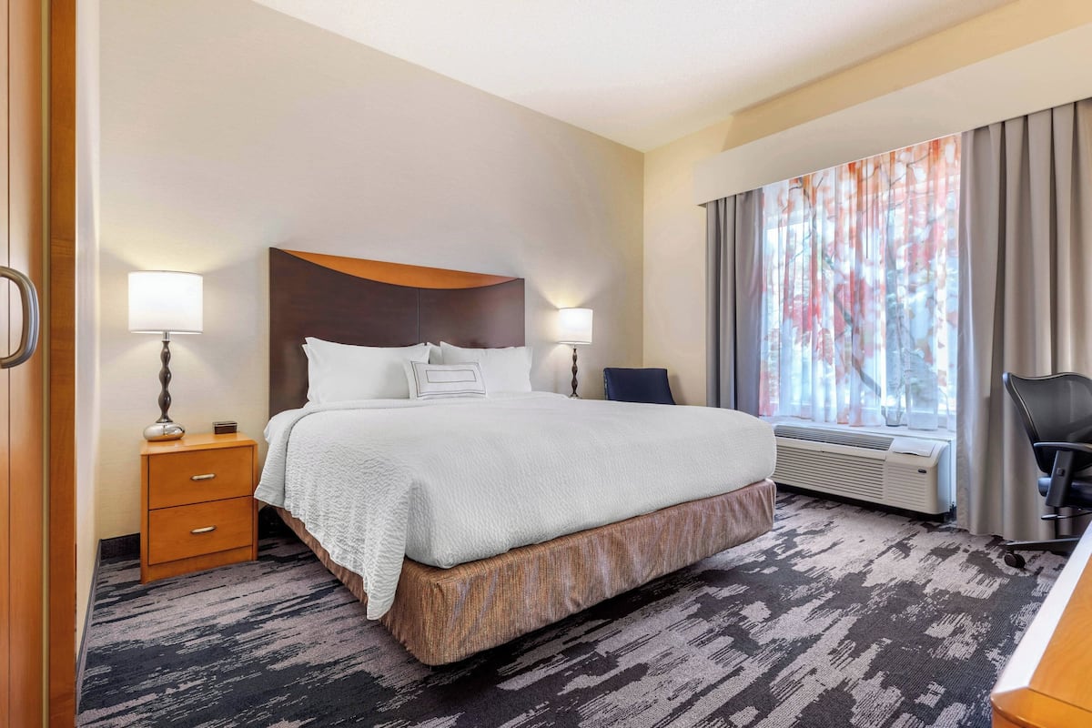 Habitación de hotel con una cama grande, dos mesitas de noche con lámparas, un escritorio y un ventanal con cortinas.