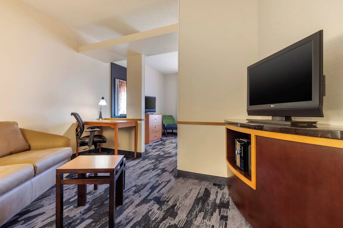 Una habitación de hotel con sofá, escritorio, televisión y piso alfombrado.