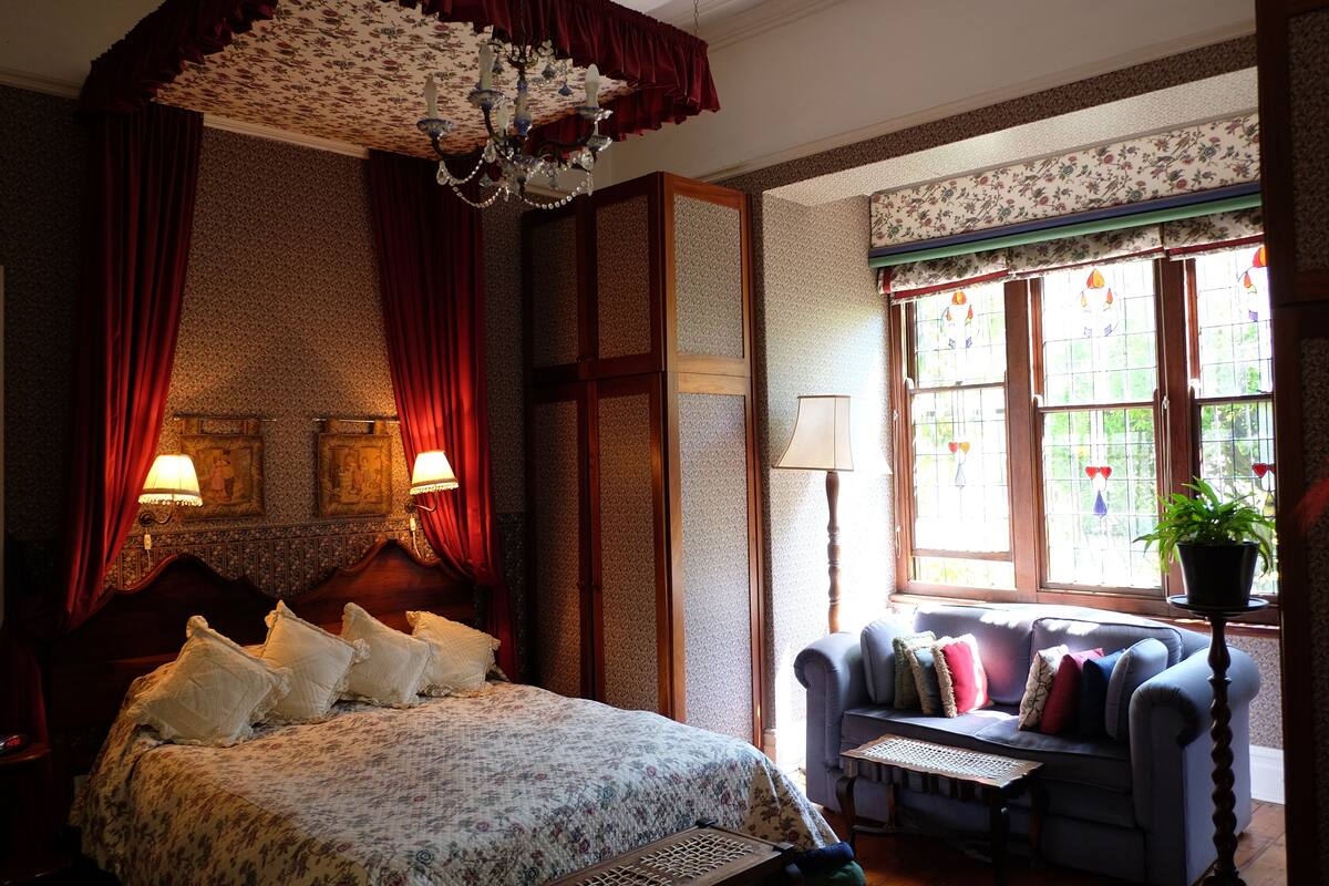 Une chambre à coucher avec un grand lit, un canapé, un lustre et une fenêtre avec des rideaux.