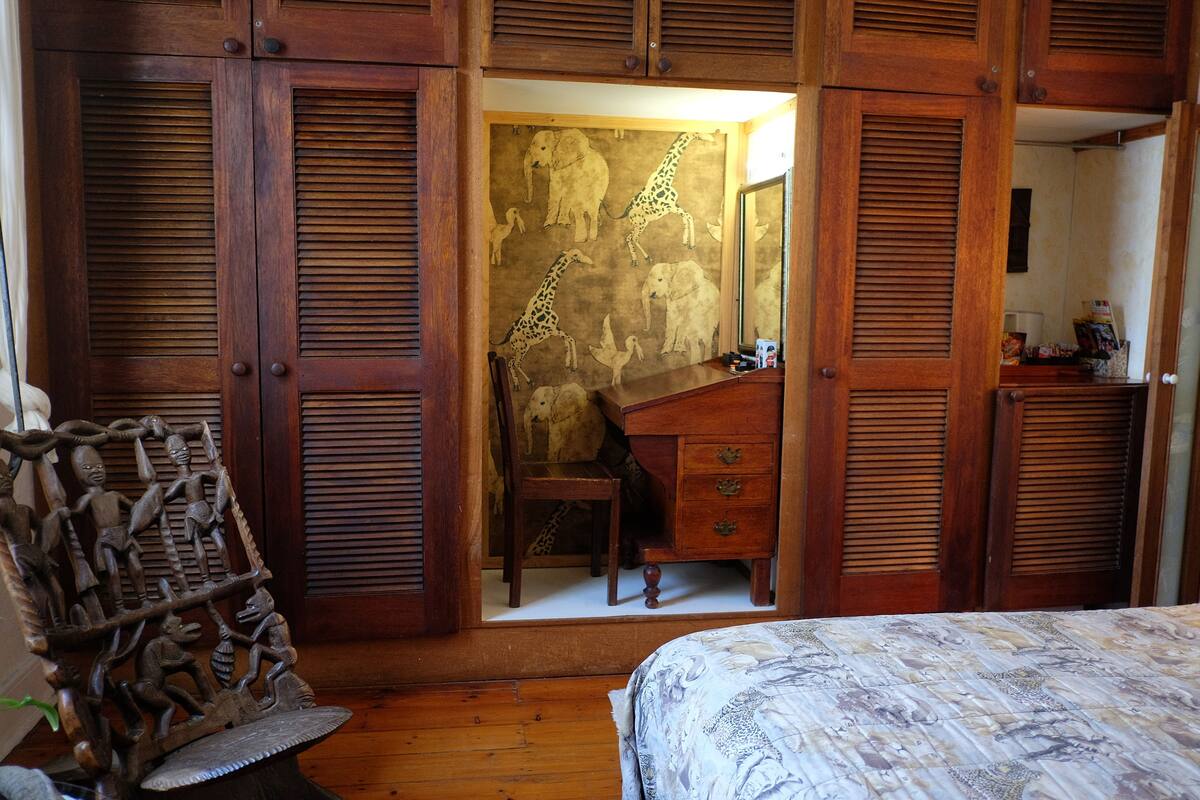 Une chambre avec des volets en bois, un lit recouvert d’une couvre-lit à motifs, un bureau avec des tiroirs et une chaise.