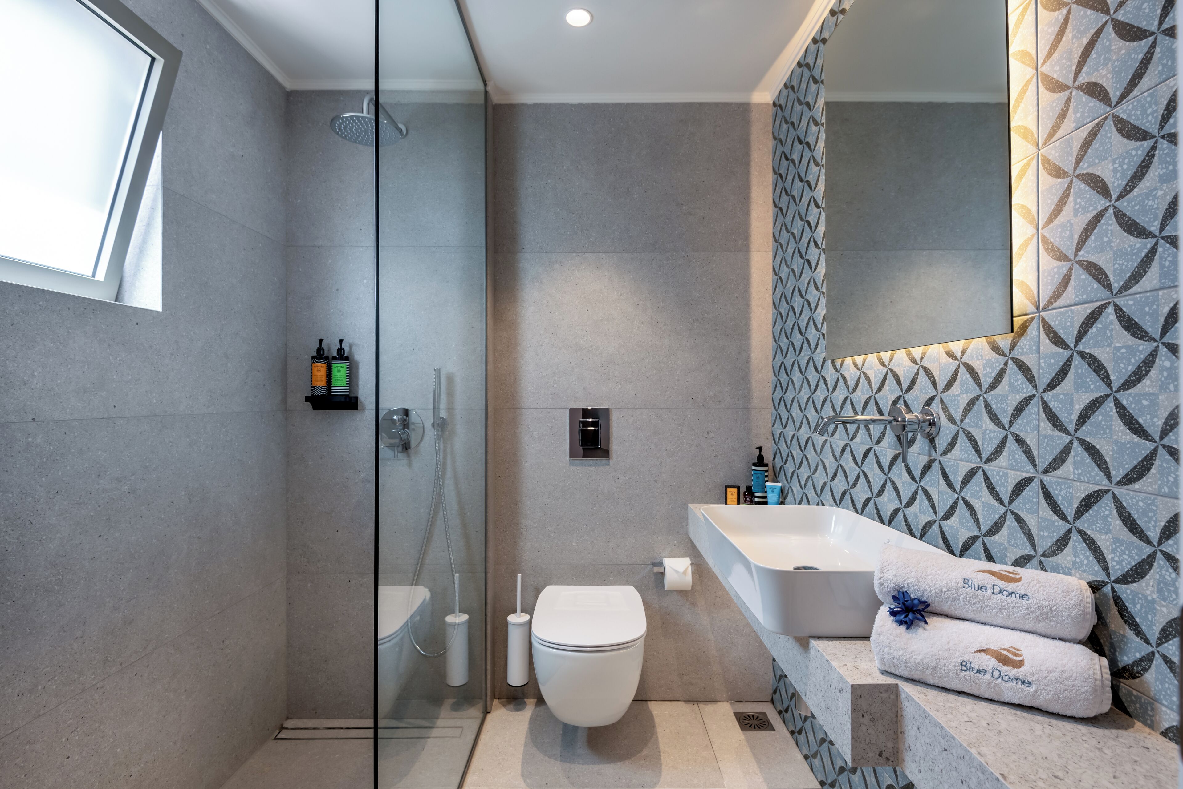 A modern bathroom with a glass-enclosed shower, a white toilet, and a large sink with a patterned backsplash.