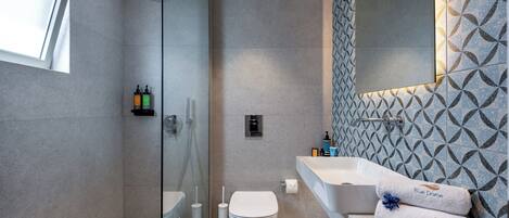A modern bathroom with a glass-enclosed shower, a white toilet, and a large sink with a patterned backsplash.