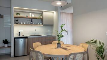 A modern kitchen with built-in appliances, a dining area with a round table and wicker chairs, and a potted plant on the table.