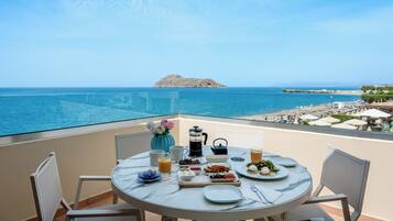 Enjoy a serene breakfast on the balcony with a stunning sea view, surrounded by fresh flowers and a delicious spread of fruits, bread, and hot beverages.
