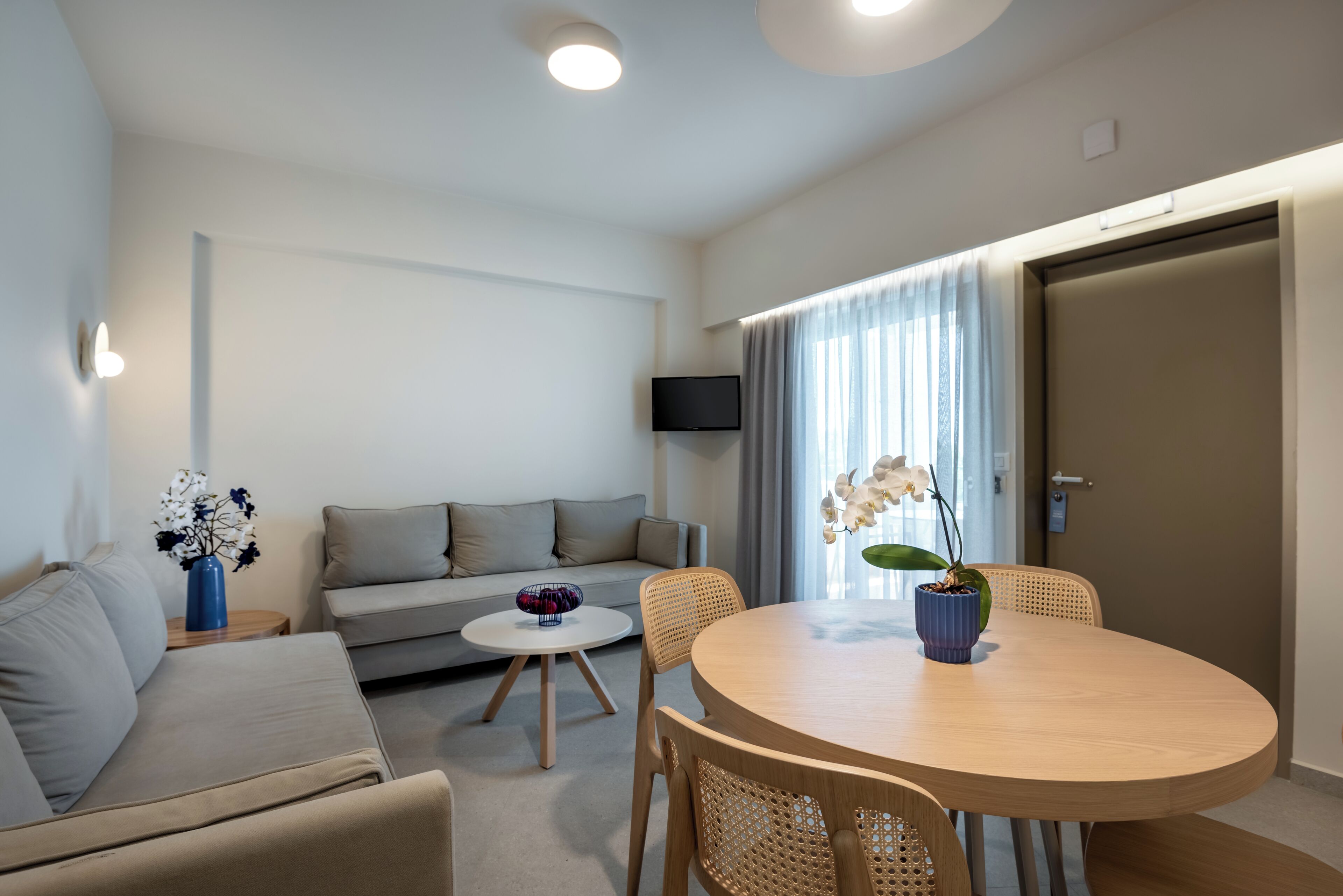 A modern living room with a sofa, a round wooden table, and a TV mounted on the wall.