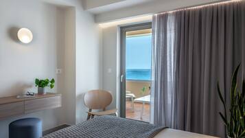 Ein modernes Hotelzimmer mit Bett, Schreibtisch mit Pflanze, Stuhl und Meerblick durch eine Balkontür.