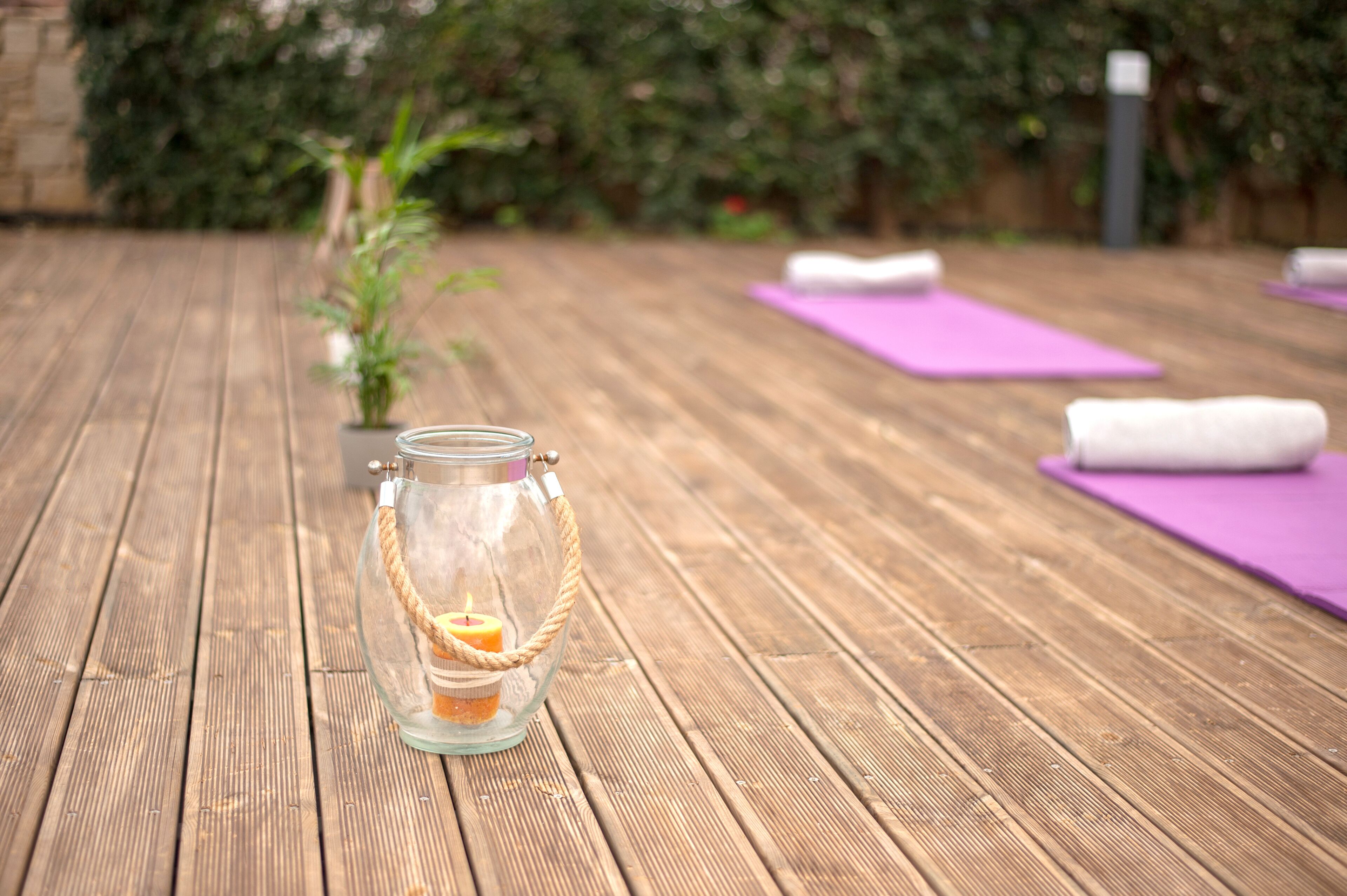 A wooden deck with a glass jar candle holder and a small potted plant.