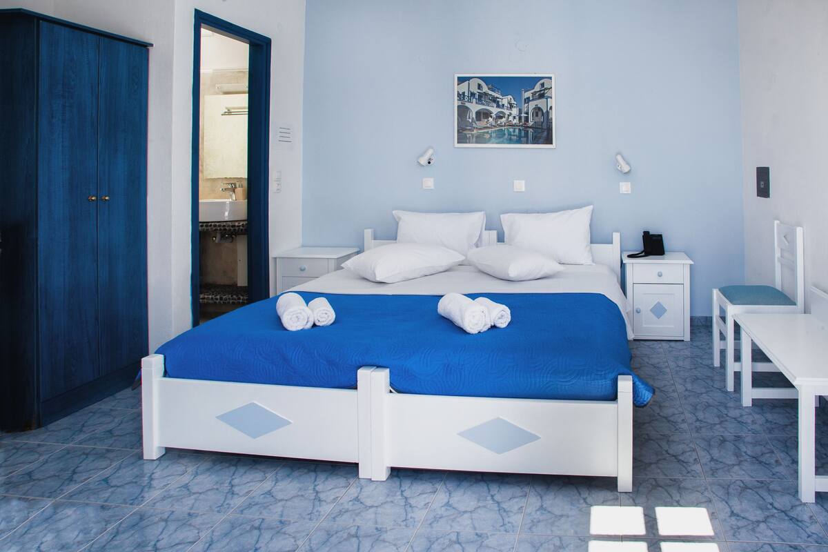 A bedroom with a bed, white nightstands, a desk, and a wardrobe.