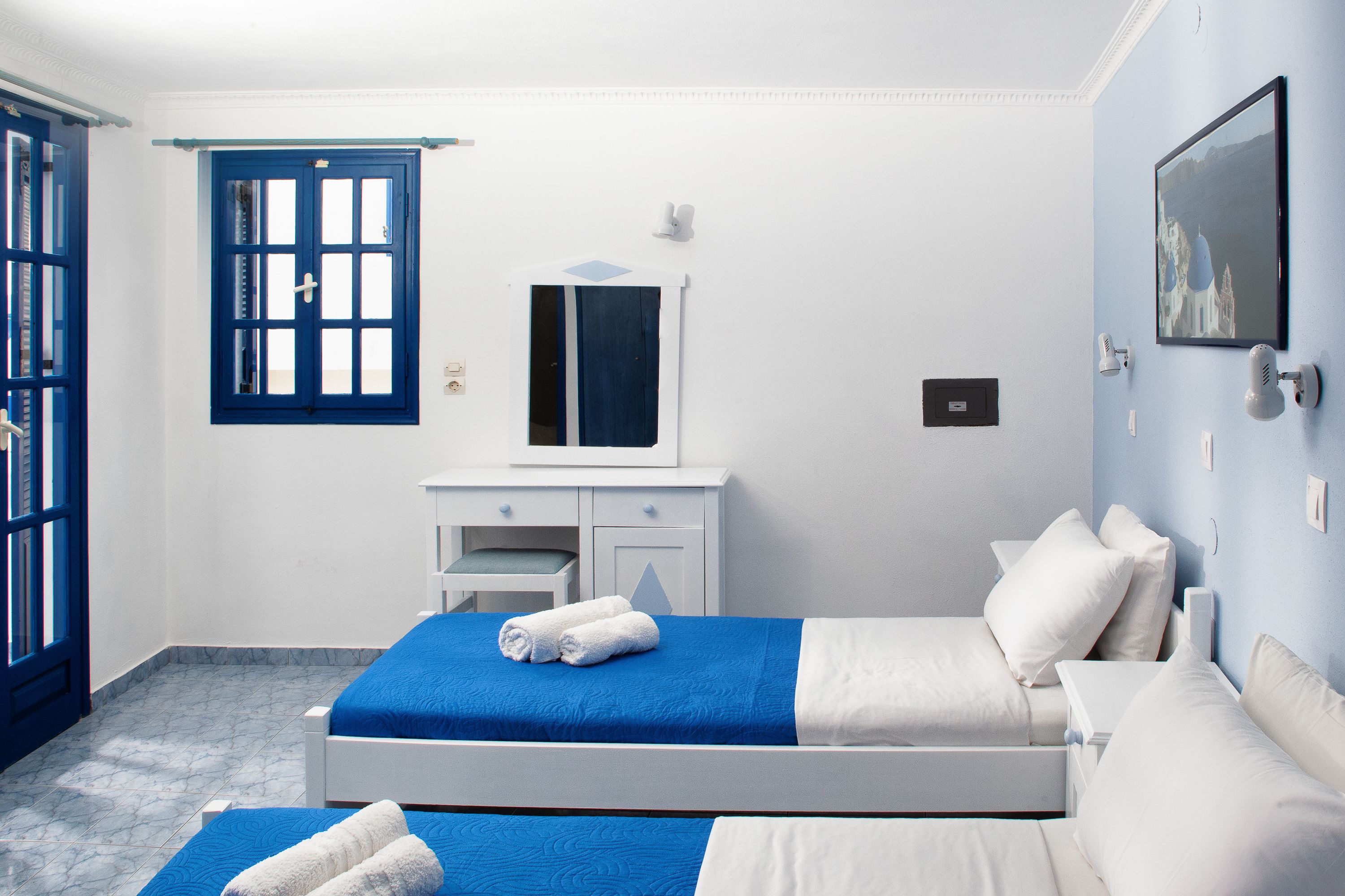 A hotel room with two beds, a white dresser, a mirror, and a window with blue shutters.