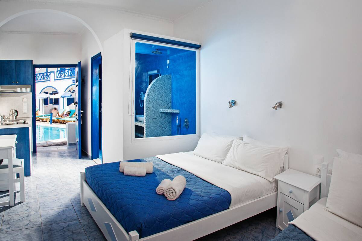 A hotel room with a large bed, a small bedside table, a nightstand, and a view of a pool area.