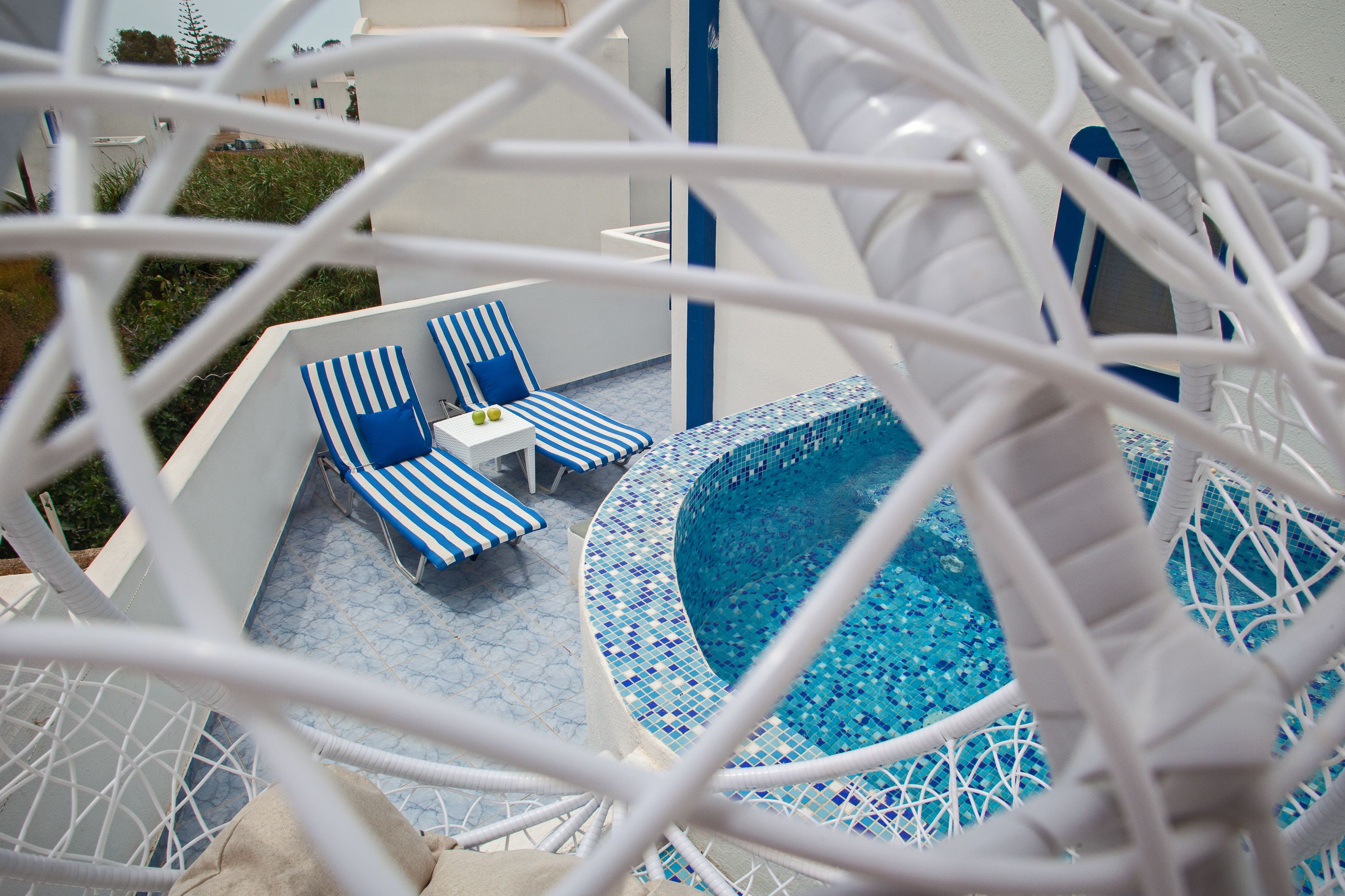 A pool area with blue and white striped lounge chairs, a small table, and a tiled pool.